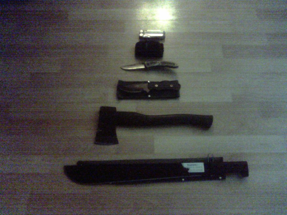 Multi-tool, folding knife, sheath, axe, and machete laid out on a wood floor