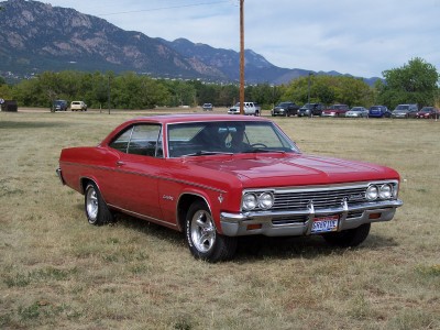 1972 Ford Ranchero - A red 1965 Chevrolet Impala coupe sits in a grassy field with mountains visible in the distance.