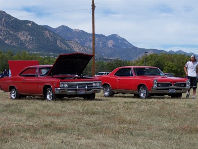 1972 Ford Ranchero - Two vintage cars are displayed outdoors with a mountainous backdrop under a partly cloudy sky.
