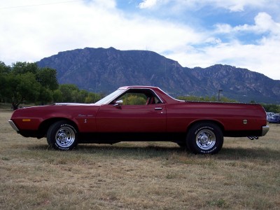 1972 Ford Ranchero - A side view of a red 1972 Ford Ranchero pickup truck with chrome wheels, parked outdoors.