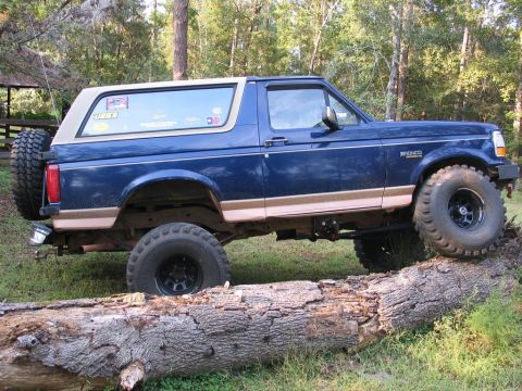 1995 Ford Bronco - This blue 1995 Ford Bronco with tan trim is shown navigating an obstacle on a wooded trail.