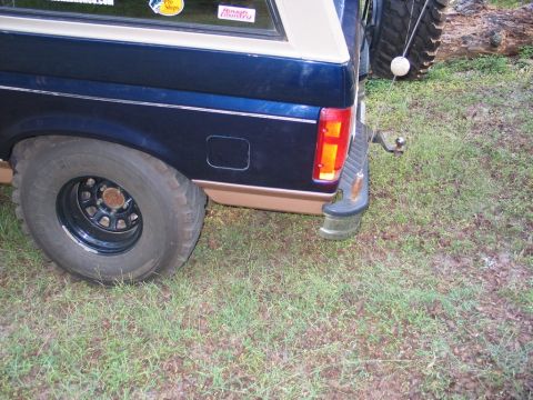 1995 Ford Bronco - The rear quarter panel of a dark blue SUV, a tan accent stripe and a visible trailer hitch.