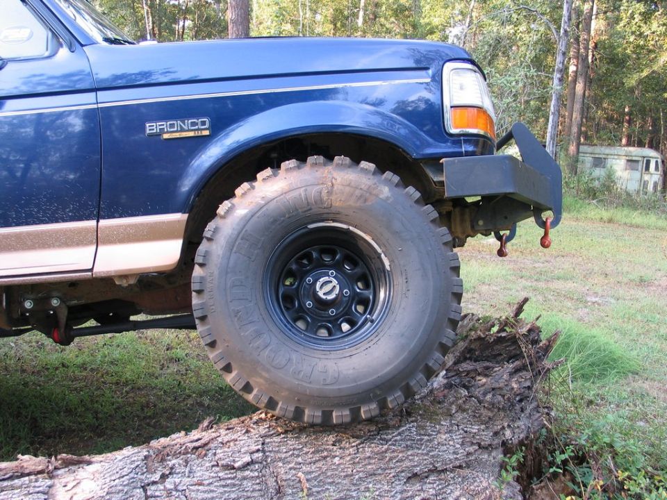 Blue 1995 Ford Bronco front fender and large tire on a log