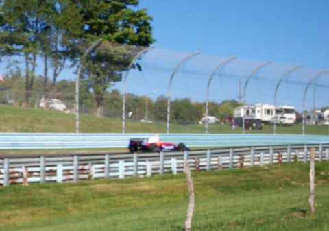 1979 Ford F-150 - A race car speeds along the track, with spectator RVs parked in the background.