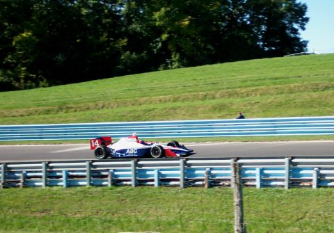 1979 Ford F-150 - A race car with the number 14 and ABC livery speeds around a track with grassy hills in the background.