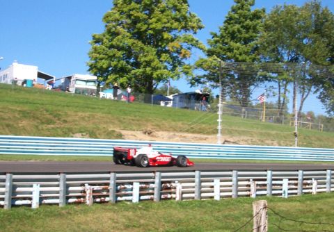 1979 Ford F-150 - A race car with 'TARGET' branding speeds down a track with spectators and trees in the background.