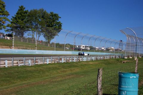1979 Ford F-150 - Race car on track with spectator RVs and trees under a clear blue sky.