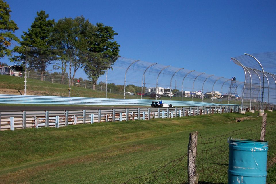 Open-wheel race car on a track with RVs and trees in the background