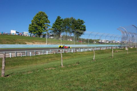1979 Ford F-150 - A race car speeds down the track on a sunny day, with spectators watching from the hillside.