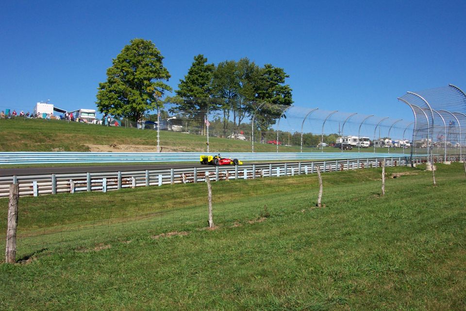 Open-wheel race car on track with spectators and RVs in background