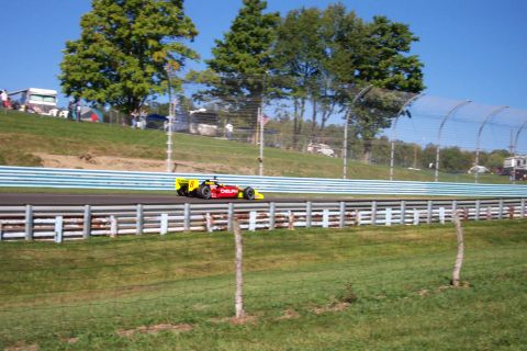 1979 Ford F-150 - A race car speeds around a track on a sunny day, with spectators in the background.