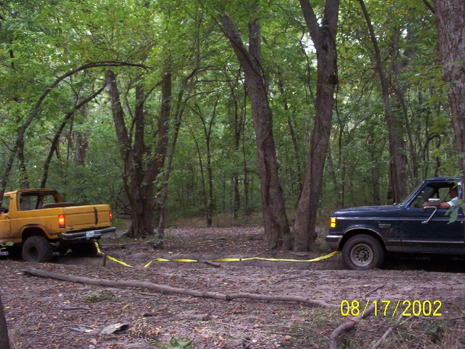Dark green 1992 Ford F-Series truck pulling a yellow Ford Bronco out of mud in a wooded area