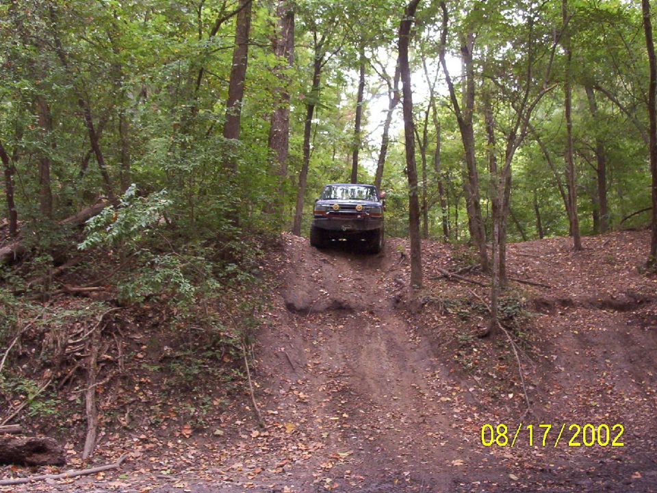 Dark blue 1992 Ford Bronco driving up a dirt hill in a wooded area