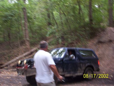1991 Ford Bronco - A Ford Bronco navigates a wooded trail with a person nearby.