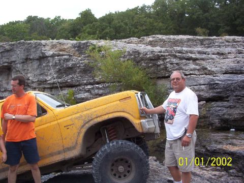 1991 Ford Bronco - Yellow Ford Bronco with large tires on rocky terrain, two men standing nearby.