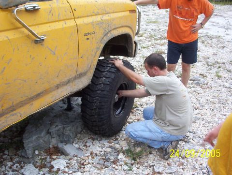1991 Ford Bronco - A man works on the tire of a yellow Ford Bronco, which is propped up on rocks.