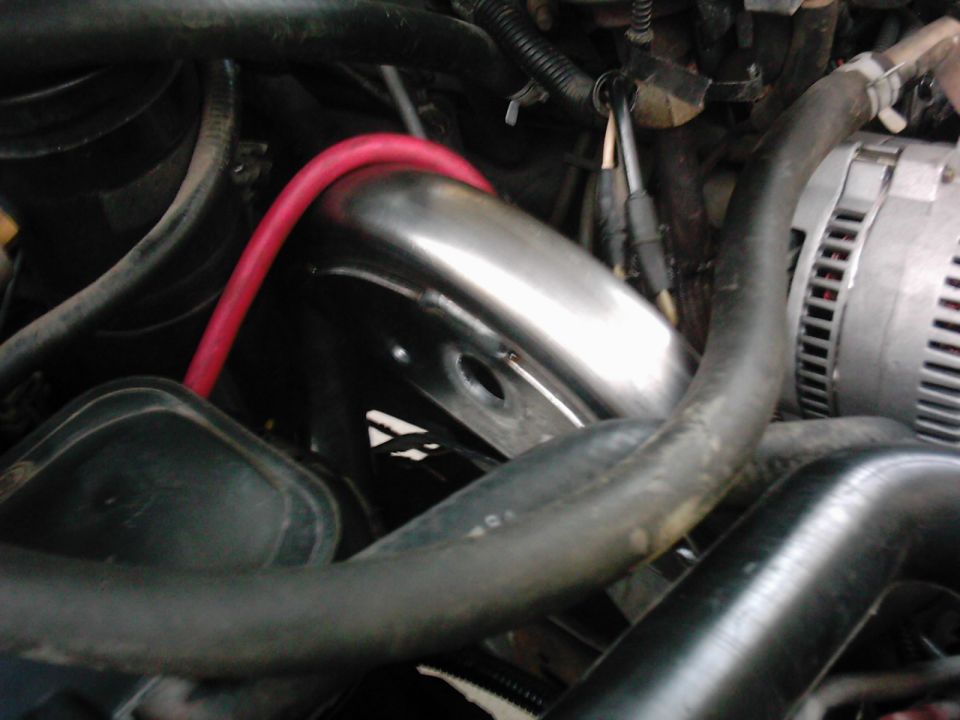 Close-up of engine bay showing alternator, exhaust pipe, and hoses