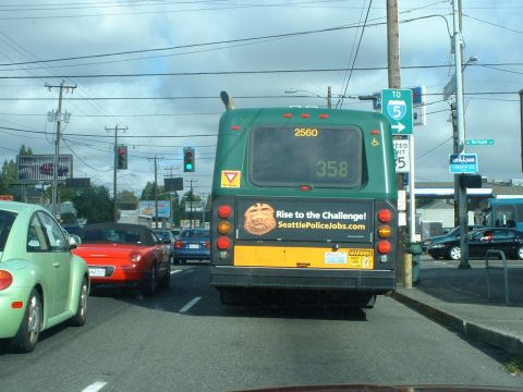 1999 Ford Crown Victoria - A green bus displays a recruitment advertisement for the Seattle Police Department, with other vehicles visible in traffic.