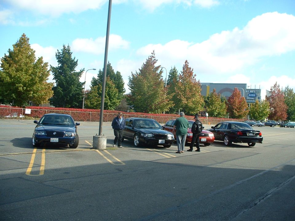 Several cars parked in a lot with people standing around them