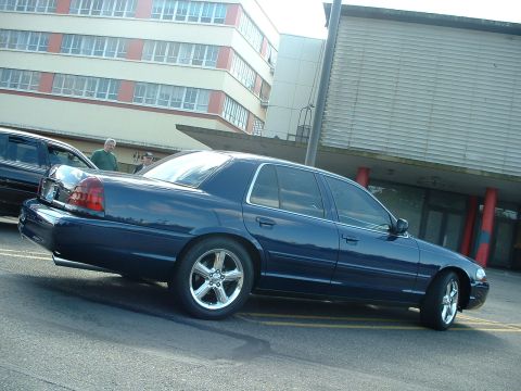 1999 Ford Crown Victoria - A dark blue sedan is seen from the side, parked next to another vehicle.