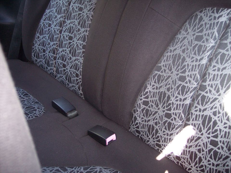 Back seat of a car with dark fabric and a geometric pattern on the seat cushions. Two seatbelt buckles are visible