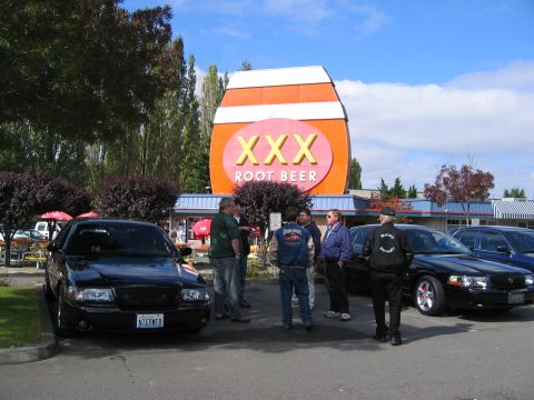 1999 Ford Crown Victoria - Several people stand around a black Ford Crown Victoria in front of a XXX Root Beer establishment.