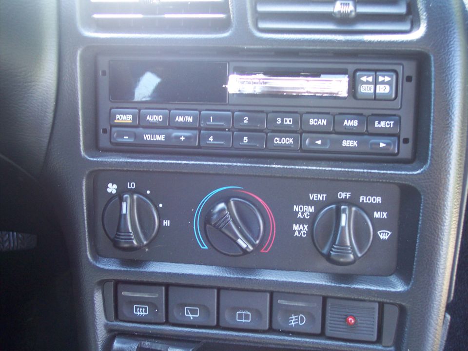 Car dashboard with radio and climate controls, including knobs for fan speed, temperature, and air direction