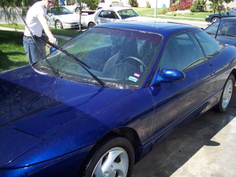 1995 Ford Probe - A person washes the windshield of a blue 1995 Ford Probe in a driveway.