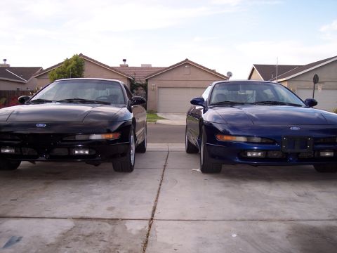 1995 Ford Probe - Two Ford Probes are parked side-by-side in a driveway, with houses in the background.