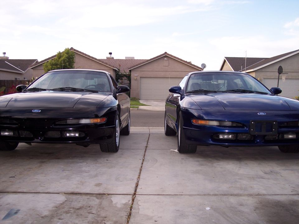 Two Ford Probes, one black and one blue, parked front-end out in a driveway