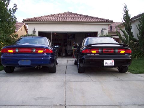 1995 Ford Probe - Two Ford Probes, a blue and a black model, are parked in front of a residential garage.