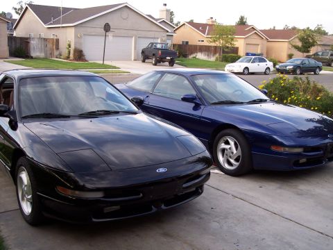 1995 Ford Probe - Two Ford Probes are parked in a suburban driveway, with houses and other vehicles visible in the background.