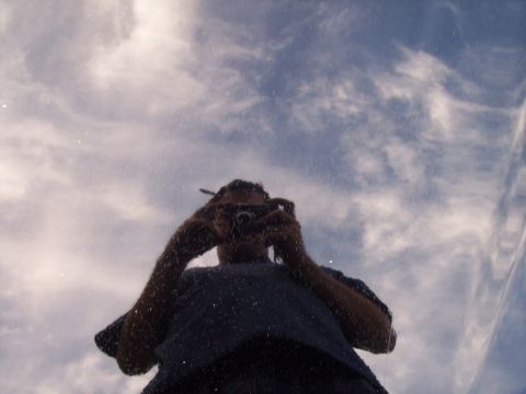 1995 Ford Probe - The reflection of a person with a camera is visible on the car's surface, set against a backdrop of clouds.