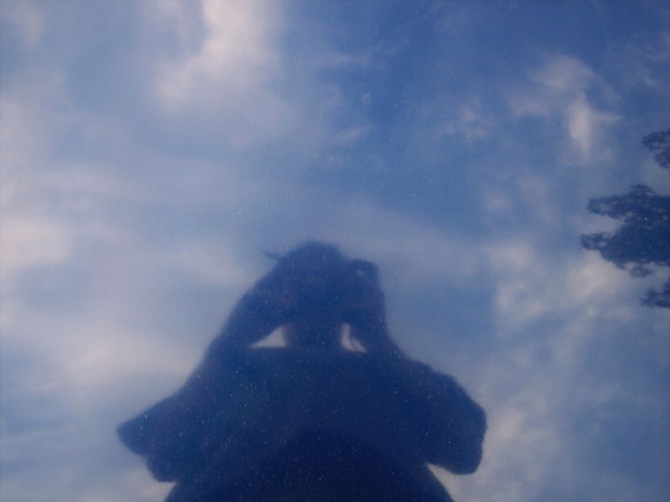 Sky and photographer reflected in glossy dark blue car paint