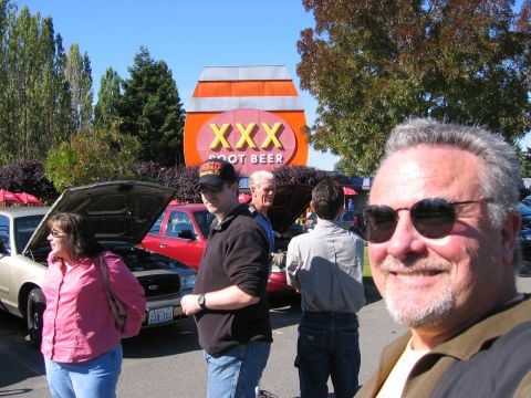 1999 Ford Crown Victoria - A group of people stand around two Ford Crown Victorias with hoods open in front of a XXX Root Beer stand.