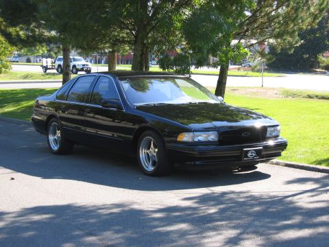 1999 Ford Crown Victoria - Black Chevrolet sedan parked on asphalt with trees and grass in the background.