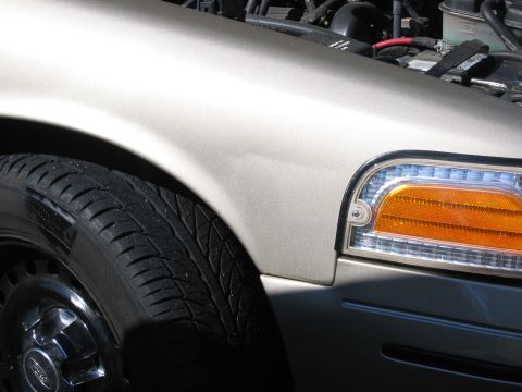 1999 Ford Crown Victoria - Close-up of the front passenger side of a 1999 Ford Crown Victoria, showing the fender, tire, and headlight assembly.