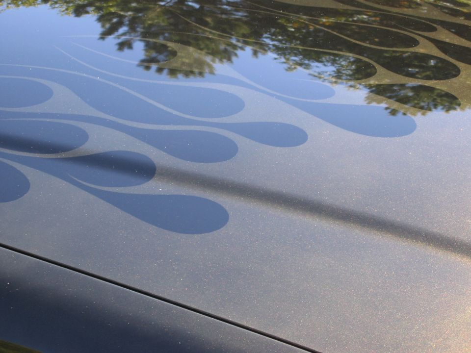 Car hood with dark flame decals. Reflection of trees in the paint