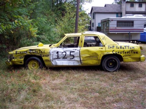 1987 Mercury Grand Marquis - This heavily damaged yellow sedan has "TOP to BOTton CONSTRUCTION" painted on its side.