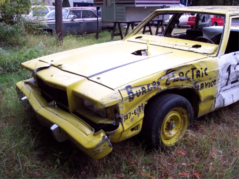 Yellow demolition derby car with crushed front end and hand-painted sponsor lettering