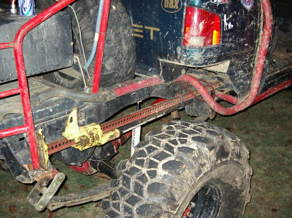 Off-road vehicle rear axle with hi-lift jack attached to frame, large mud tire visible
