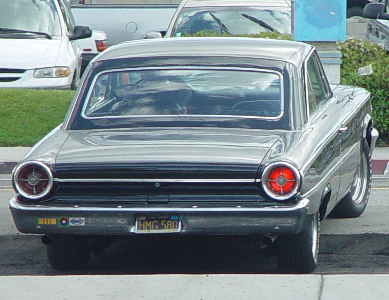 Rear view of a 1960s coupe with round taillights and a black roof. License plate reads HMG 580
