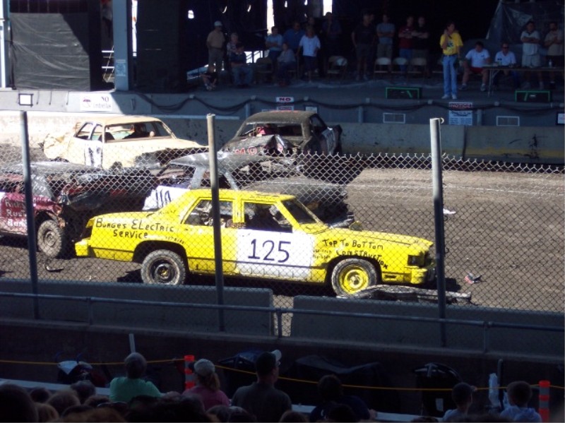 Yellow #125 demolition-derby sedan among wrecked cars in an arena