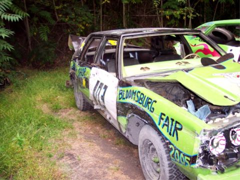 1987 Mercury Grand Marquis - This heavily damaged sedan, likely prepared for a demolition derby, displays "Bloomsburg Fair" and "2005" painted on its exterior.