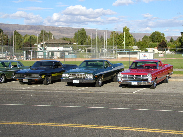 Row of classic Ford Ranchero coupe-utility pickups parked at a show beside a ballfield