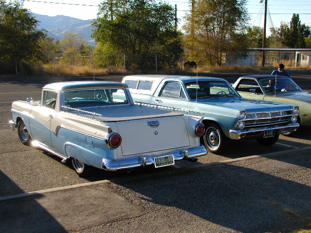 White and blue Ford Ranchero, rear three-quarter view, parked beside a blue sedan