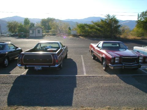 1967 Ford Ranchero - Two pickup trucks are parked side-by-side in a lot with mountains in the background.