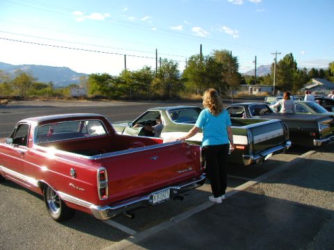 1967 Ford Ranchero - A red 1967 Ford Ranchero is parked next to other vehicles, with a woman standing between them.