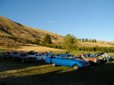 1967 Ford Ranchero - A collection of classic vehicles gathered on a grassy field under a clear blue sky.