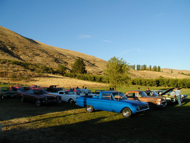 Blue 1960 Ford Ranchero with chrome wheels parked on grass, side view